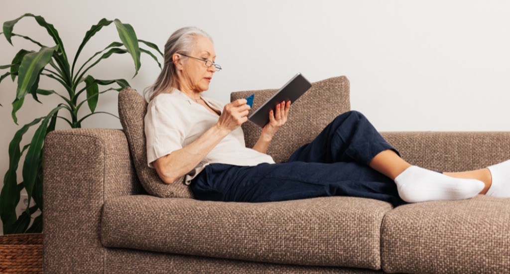 Kvinde der sidder i sofa og ordner noget med sit betalingskort på en tablet